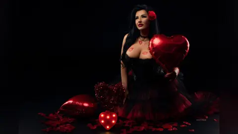 MissyJolie poses in a black lace bustier and red tulle skirt, holding a large red heart balloon against a black background.