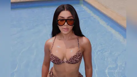 Stylish woman in leopard print bikini and oversized sunglasses relaxing by a sunny swimming pool.