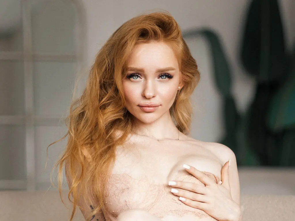 Beautiful redhead woman in delicate lace lingerie posing with a soft, romantic expression in a bright studio.