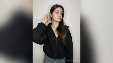 Young woman in a black zip-up hoodie posing against a white background with a thoughtful mood.