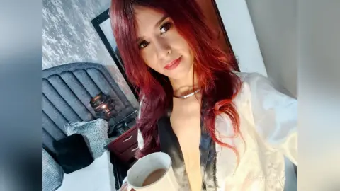 Red-haired woman in a white satin robe relaxing in a bedroom with a cozy, serene mood.