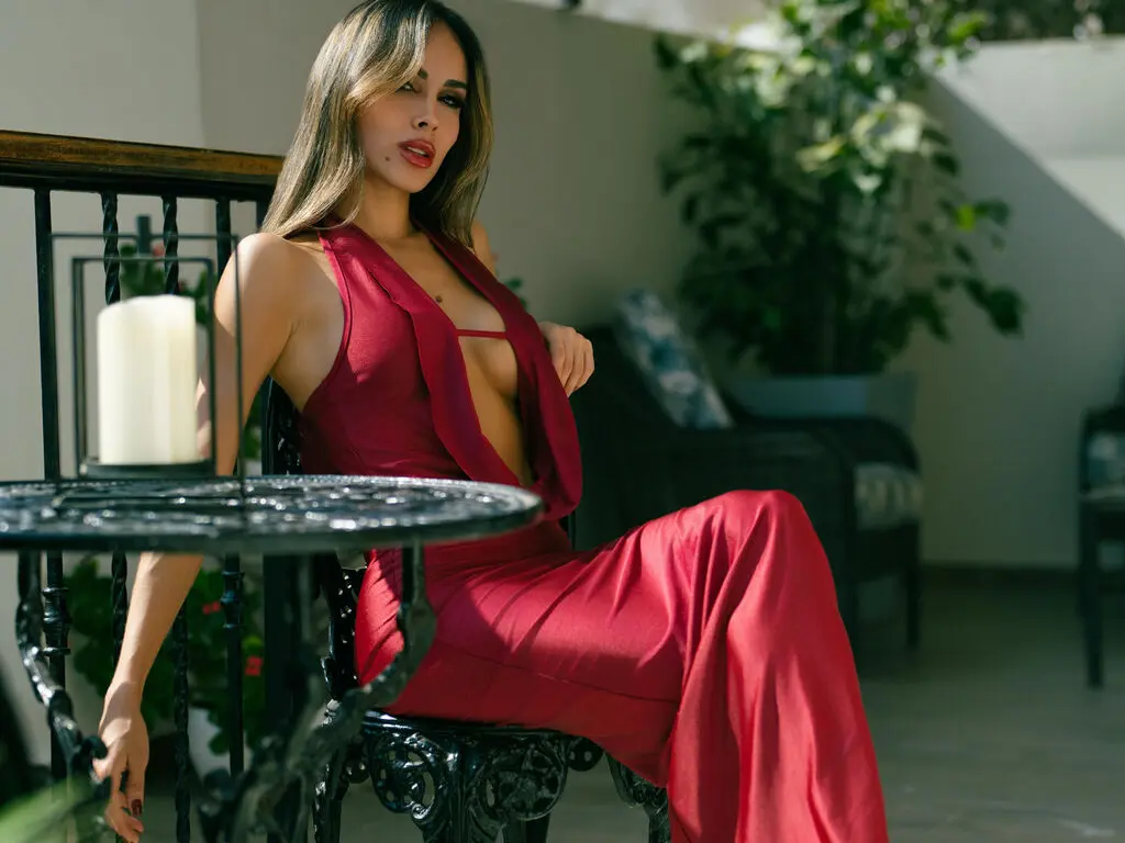 Elegant woman in a red sleeveless evening gown sitting on a patio terrace near a candlelit table.