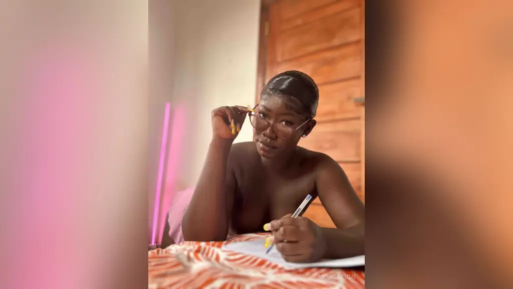 MonaReign — Young woman with glasses relaxing on a bed in a warm, cozy indoor setting.