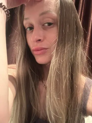 Blonde woman in a grey tank top posing for a casual indoor selfie with a relaxed mood.