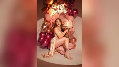 Glamorous woman in a champagne satin dress celebrating her birthday with pink balloons and a cake.