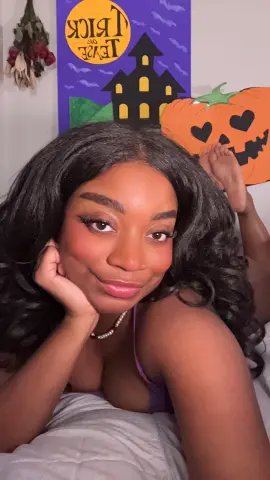 Smiling woman in a purple top posing in front of spooky Halloween decorations and a pumpkin cutout.