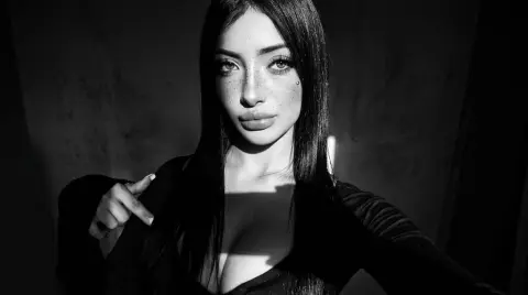 Moody black and white portrait of a freckled woman in a black top against a dark background.
