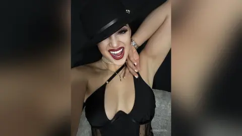 Smiling woman in a black halter top and wide-brimmed hat posing against a dark background.