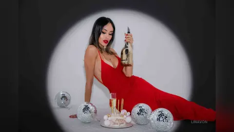 Glamorous woman in a red evening gown celebrating New Year's Eve with champagne and disco balls.