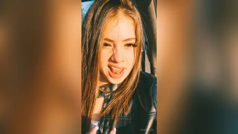 MiaBolson — Smiling young woman with long brown hair wearing a black leather jacket in warm golden hour sunlight.