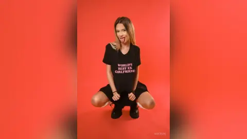 Playful young woman in a black graphic t-shirt posing against a vibrant red background.