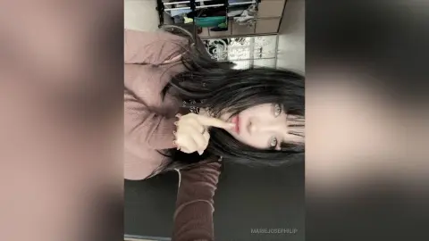 MarieJosePhilip looks at the camera with long black hair, wearing a brown long-sleeved top while resting her finger against her lips.