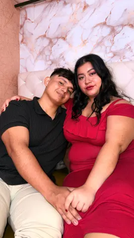 Happy young couple in casual outfits cuddling on a bed against a marble patterned wall.