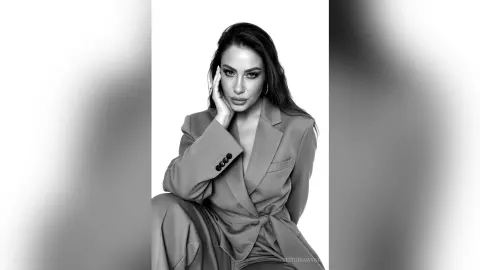 Elegant woman in a tailored blazer posing for a sophisticated black and white studio portrait.