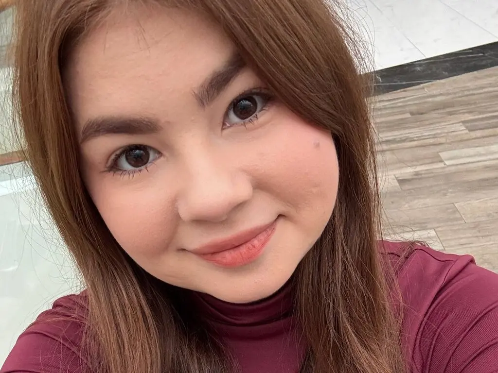 RosaAmour smiles close up, showing her long brown hair and wearing a maroon turtleneck top.