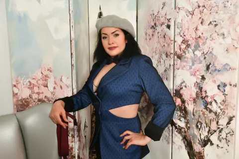 Elegant woman in a blue patterned blazer and black top posing against a floral art screen background.