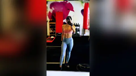 Fit woman in pink sports bra and blue leggings taking a mirror selfie in a bright gym setting.