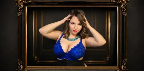 Young woman in blue lace lingerie and turquoise necklace posing confidently in a vintage gold frame.