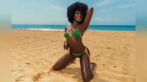Smiling Black woman in a green crochet bikini posing on a sunny tropical beach.