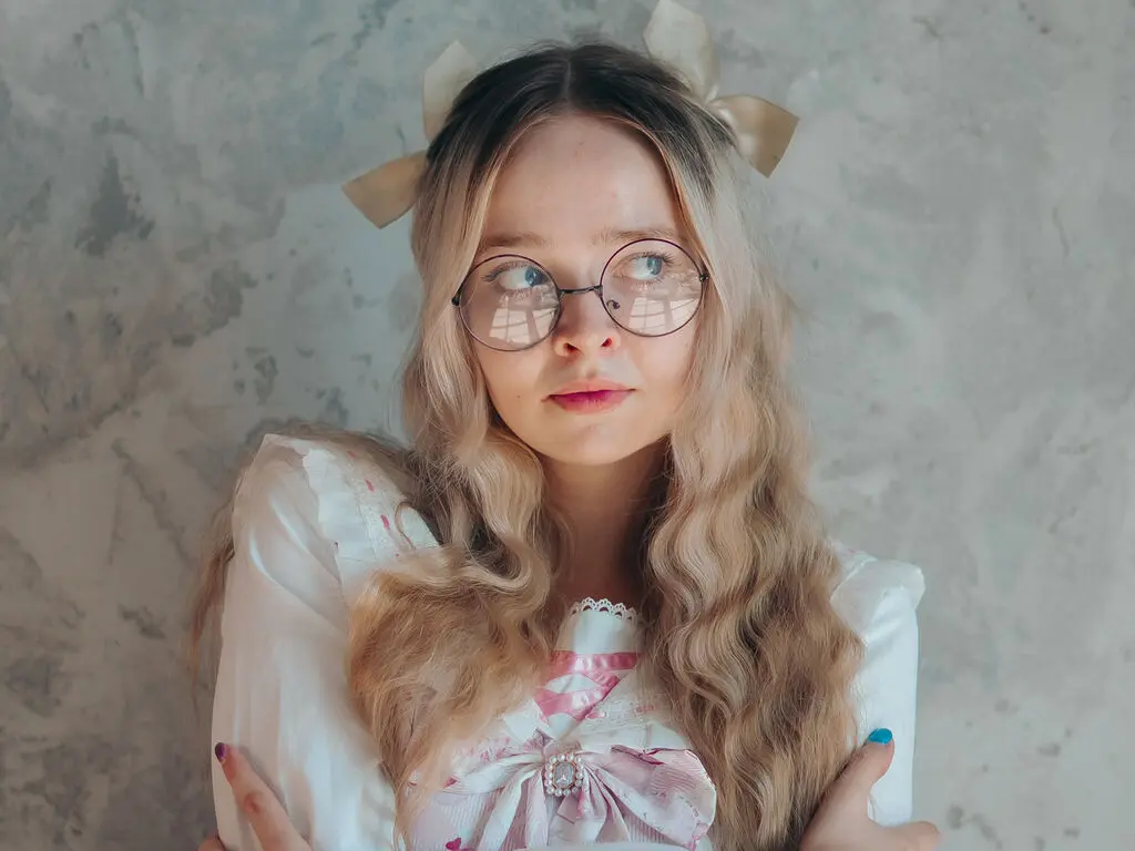 Dreamy portrait of a blonde girl with glasses and hair bows wearing a white vintage lace blouse.