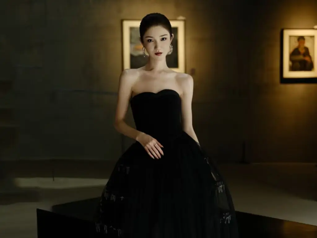 Elegant woman in a black strapless evening gown posing in a moody, dimly lit art gallery setting.