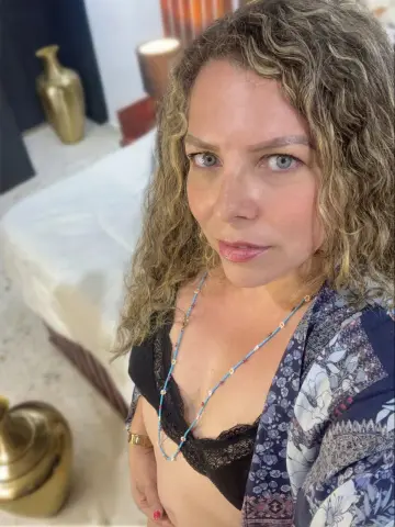Woman with curly hair wearing a floral robe and black lace bra in a bright indoor setting.