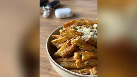 Crispy golden french fries topped with grated parmesan cheese in a rustic ceramic bowl on a wooden table.