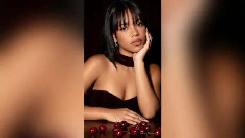 Elegant woman in a burgundy velvet dress posing with cherries in a moody, dark studio setting.