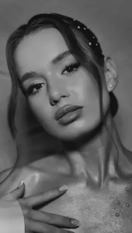 Close-up black and white portrait of a glamorous woman with glowing skin and elegant makeup looking at camera.