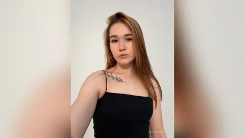 JaneBarbrick poses in a black tank top, showing off her long brown hair and a small leaf tattoo on her collarbone.