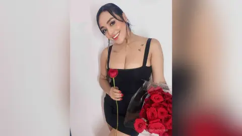 Smiling woman in a black cocktail dress holding a bouquet of red roses against a white background.