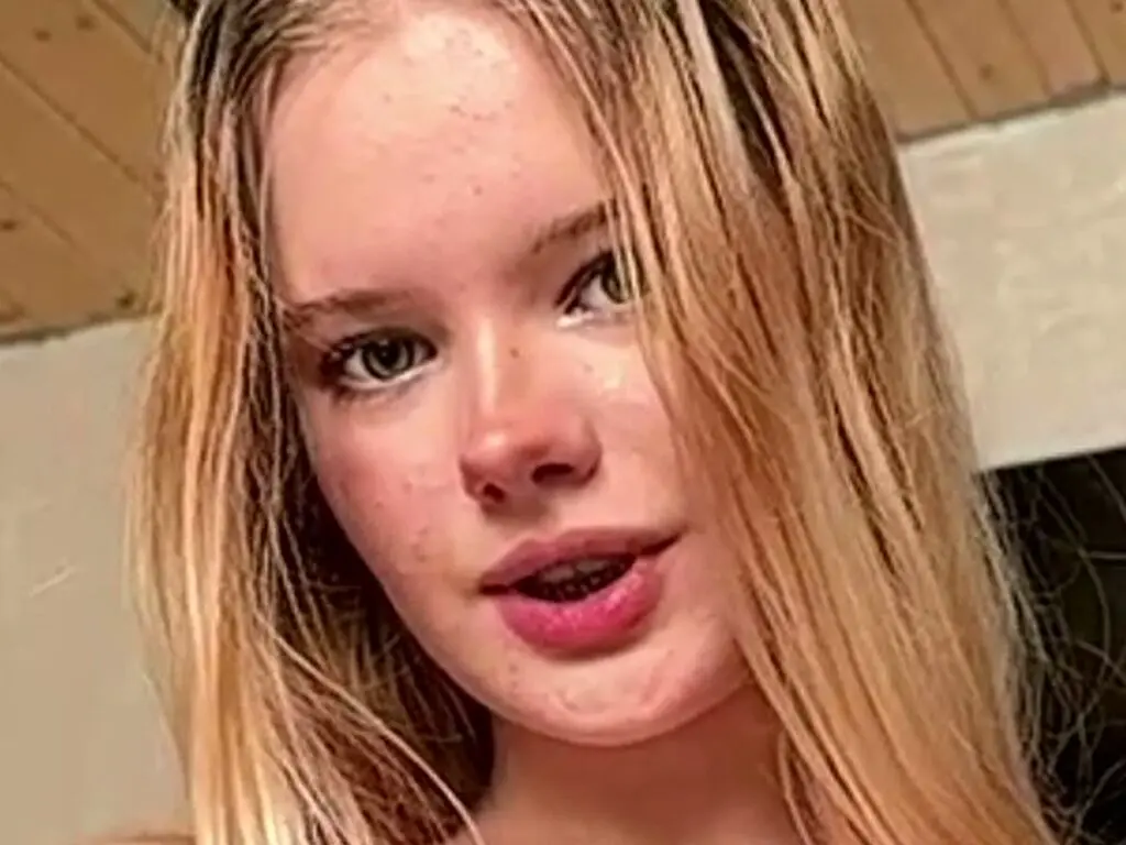 Close-up portrait of a blonde girl with freckles looking at the camera in a bright indoor setting.