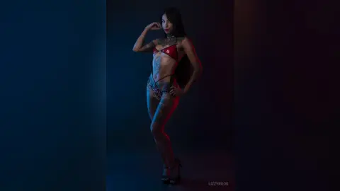 Tattooed woman in a red bikini posing confidently in moody, cinematic blue and red studio lighting.