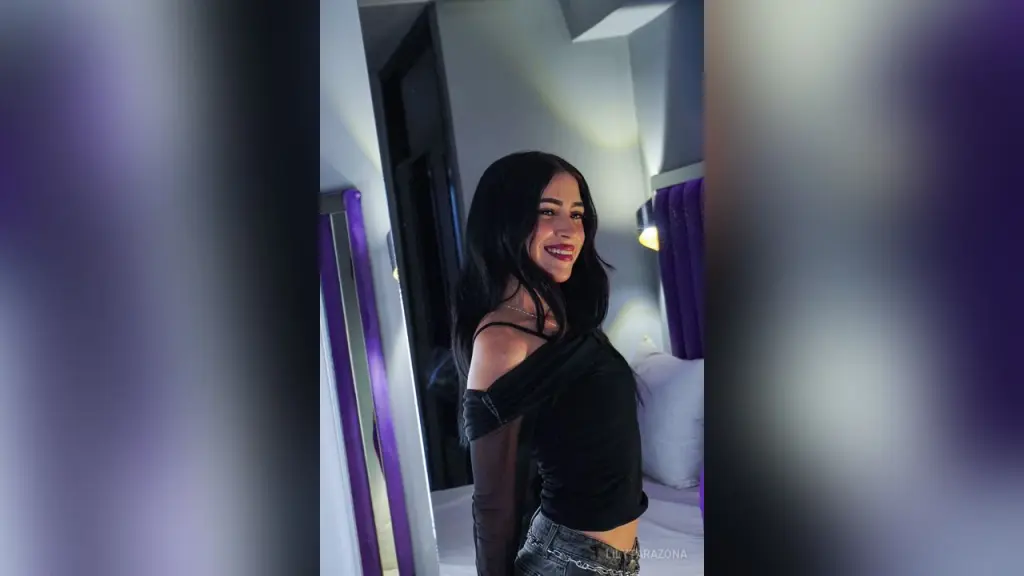 LilyTarazona poses with her hand in her long black hair, wearing a black sheer long-sleeve top.