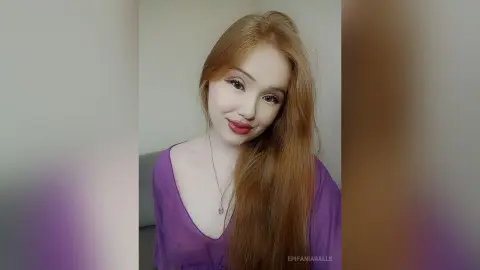 EpifaniaRalls smiles while wearing a purple v-neck top, showing her long red hair and silver necklace against a plain background.