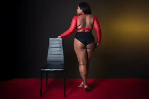 Curvy woman in a red long-sleeve crop top and black high-waisted briefs posing against a dark studio backdrop.
