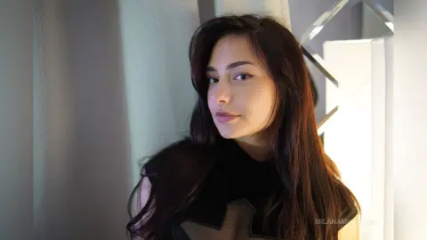 Young woman with long dark hair in a black outfit posing in soft, warm indoor lighting.
