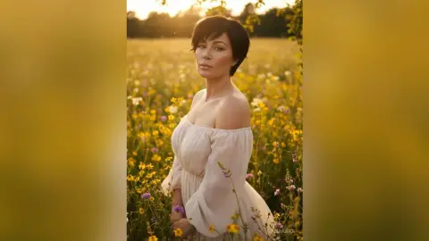 Dreamy portrait of a woman in a white off-the-shoulder dress standing in a sunny wildflower meadow at sunset.