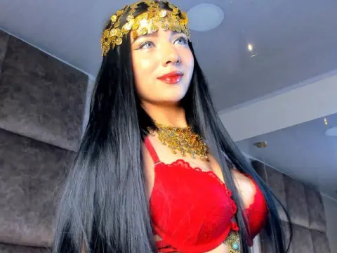 Young woman with long black hair wearing a gold coin headpiece and red lace outfit in a modern room.