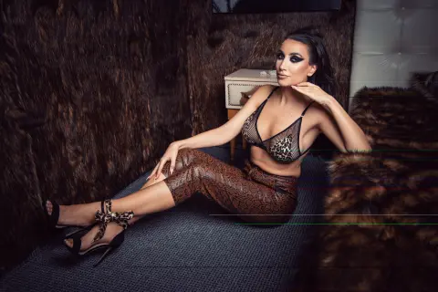 Glamorous woman in leopard print bikini and trousers lounging on a textured rug in a moody, luxury setting.