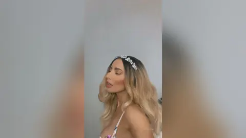 Katia wears a sparkly headband and a white lace top while looking away from the camera.