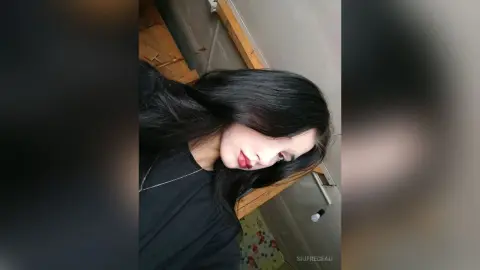 Young woman with long dark hair wearing a black t-shirt in a casual indoor setting.