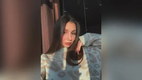 Young woman in a cozy patterned sweater posing in warm sunlight for a soft, aesthetic portrait.
