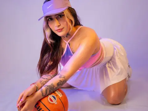 Young woman in pink sports bra and white skirt posing with a basketball in soft purple lighting.