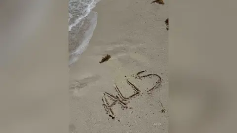 The word AUS written in the sand on a peaceful beach with gentle ocean waves washing ashore.
