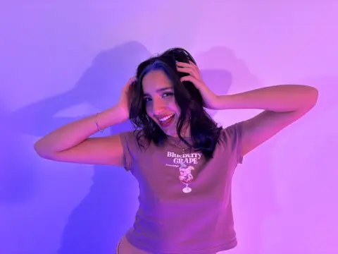 Smiling young woman in a graphic t-shirt posing against a purple neon lit wall in a moody studio setting.