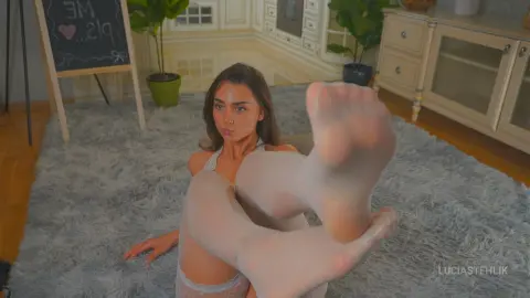 Young woman in white lace lingerie relaxing on a grey shag rug in a cozy, bright bedroom.