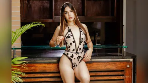 Young woman in a floral lace bodysuit posing in a modern kitchen setting with a confident mood.