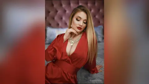 Elegant woman in a red satin dress and silver necklace posing glamorously on a bed.