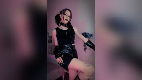 LorenLoiss poses in a black tank top and leather skirt with black gloves and a choker, showing off her tattoos.